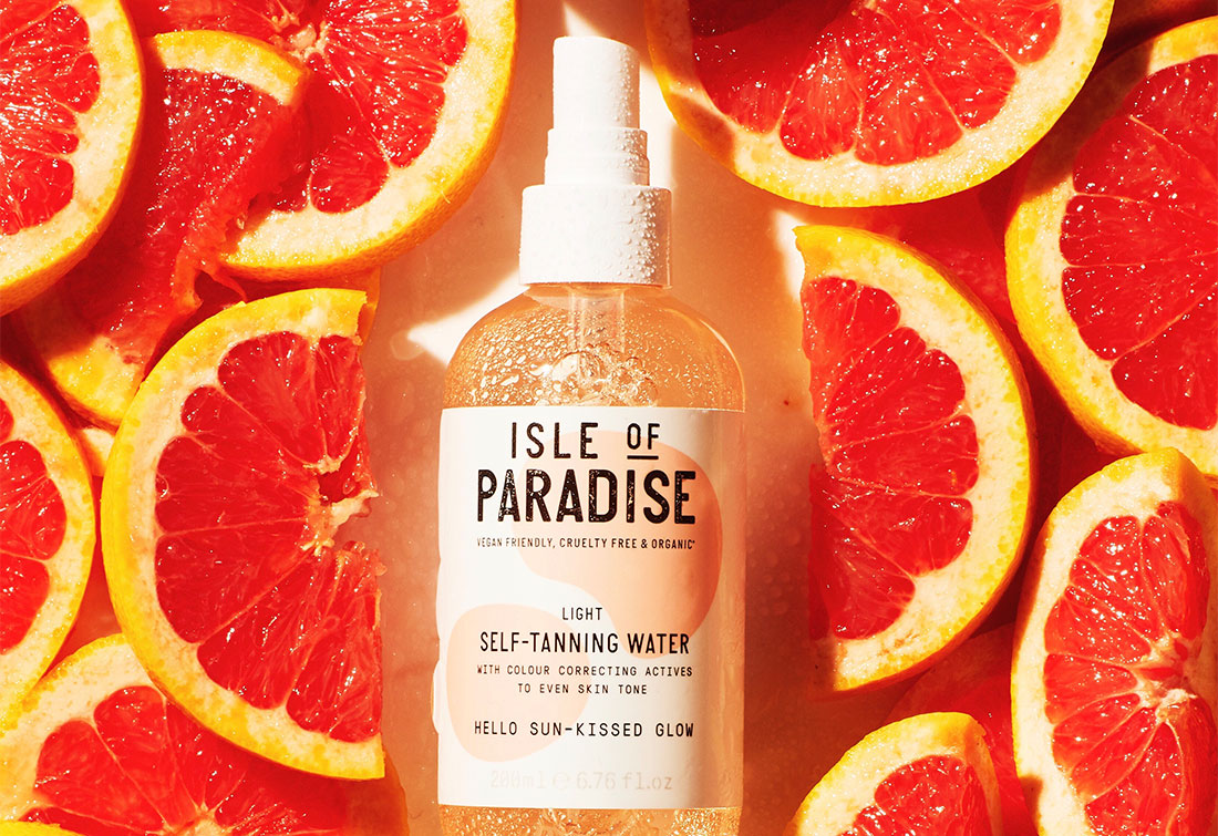 Light self tanning water bottle lying flat between freshly cut oranges